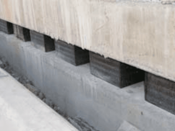 Nahaufnahme einer elastischen Entkopplung, die durch rechteckige schwarze Elastomerlager zwischen Wandscheibe und Trägerrost abgestützt ist.