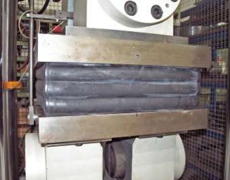 Nahaufnahme einer Industriemaschine mit Metallwalzen und einem Stahlrahmen, die wahrscheinlich zur Verarbeitung oder Formung von Materialien in einer Fabrik verwendet wird.