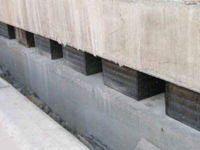 Reihe schwarzer, rechteckiger Elastomer-Brückenlager zwischen Betonbrückensegmenten zur strukturellen Unterstützung, ideal für Anwendungen, die elastische Gebäudelagerung erfordern.